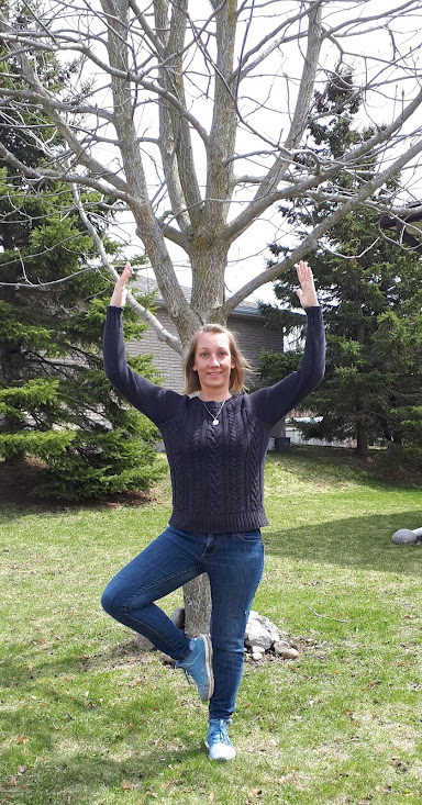Emma standing in yoga's tree pose in front of tree